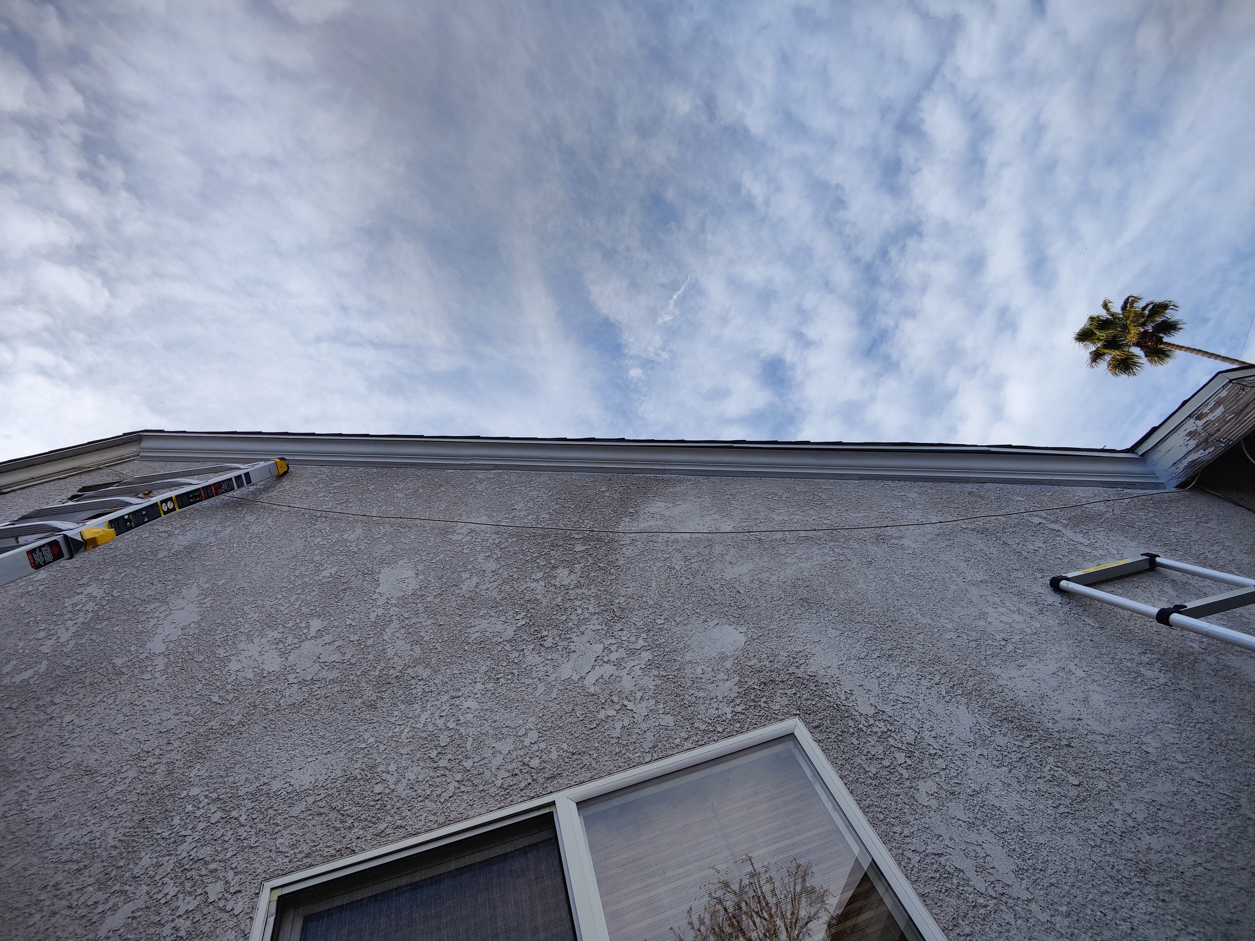 Ladders set up on both sides of house for fascia repair in progress