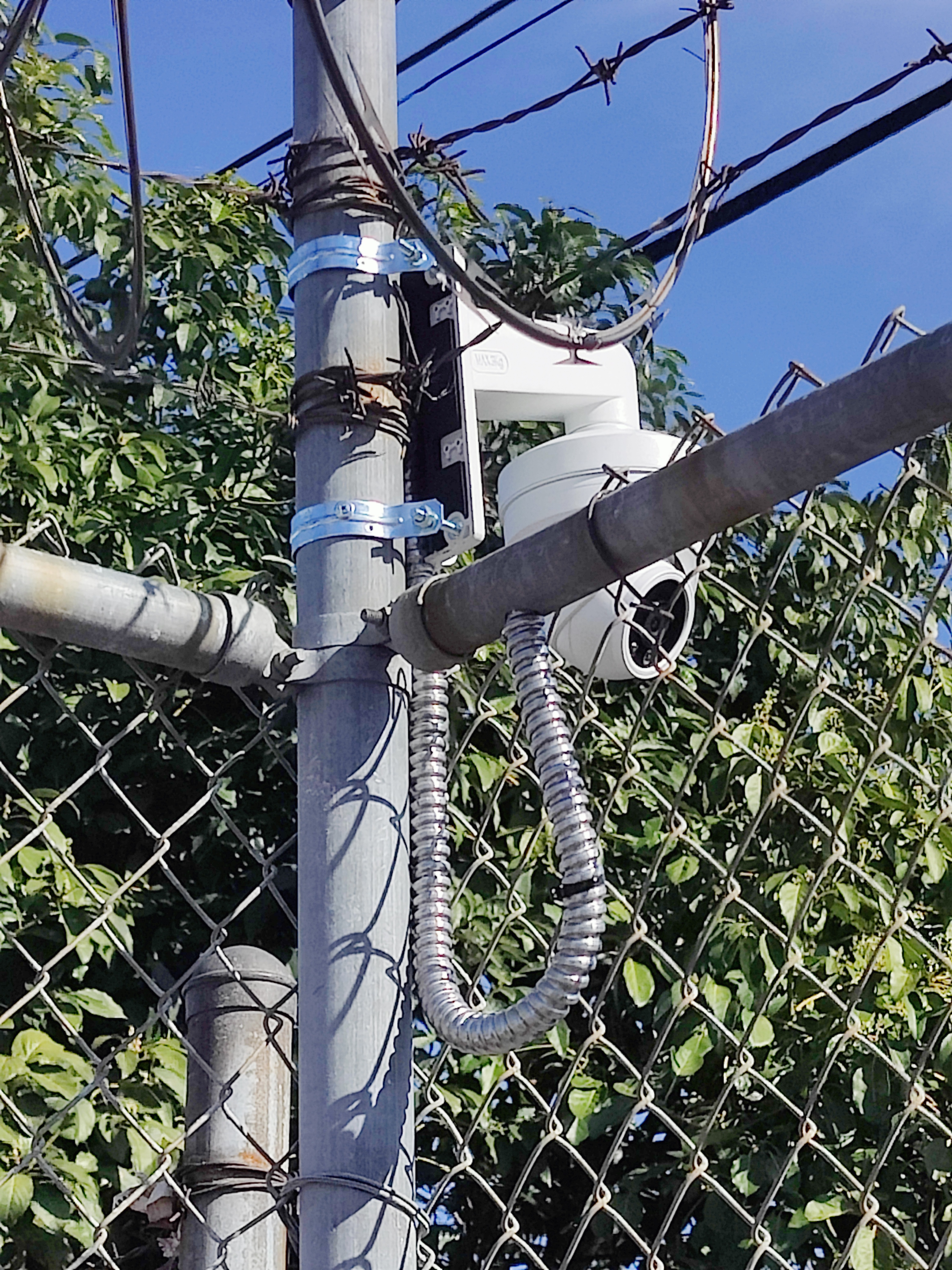PTZ camera mounted with armored conduit on chain-link fence post