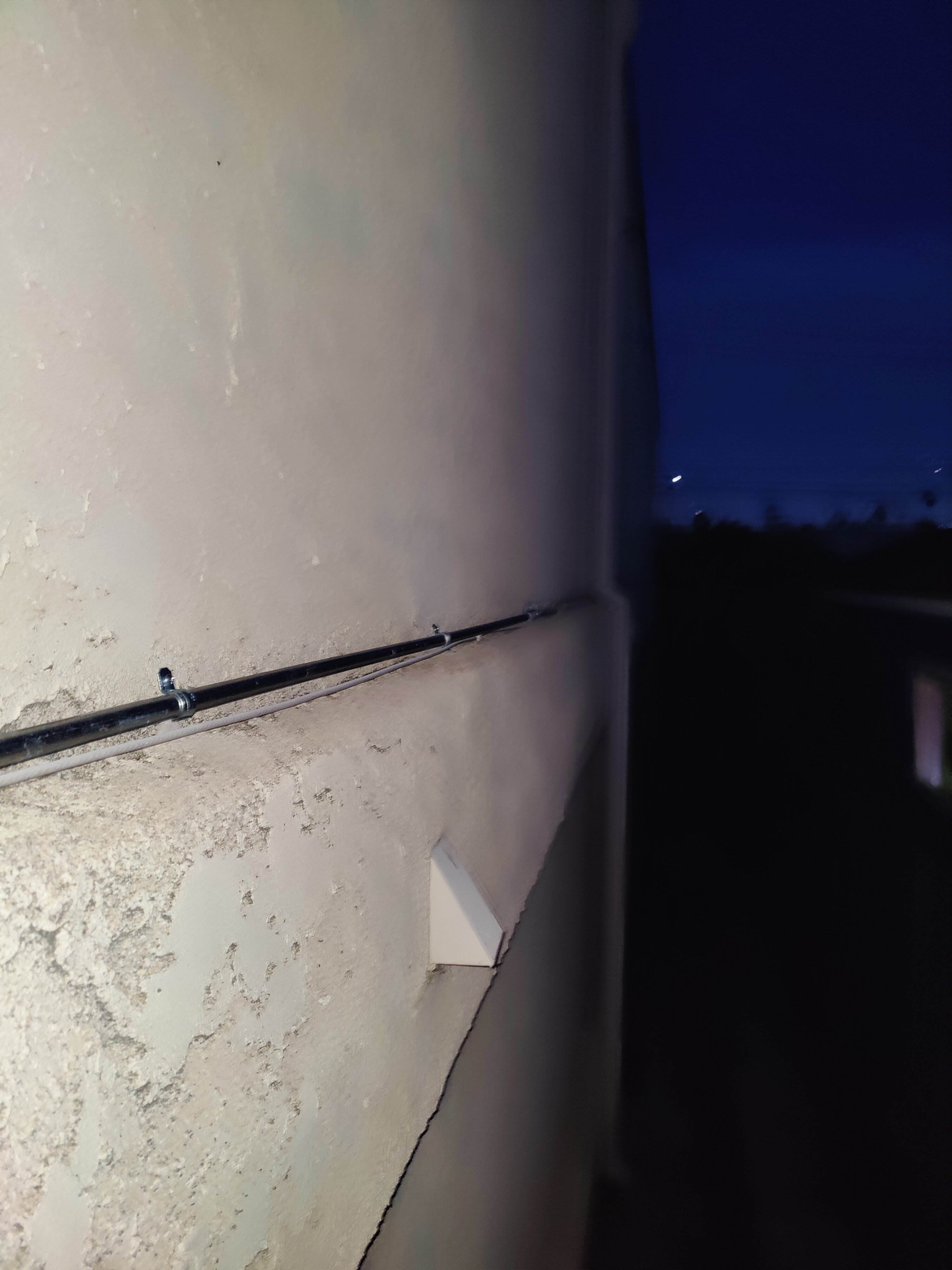 Exterior cable run on stucco wall for security camera feed at dusk