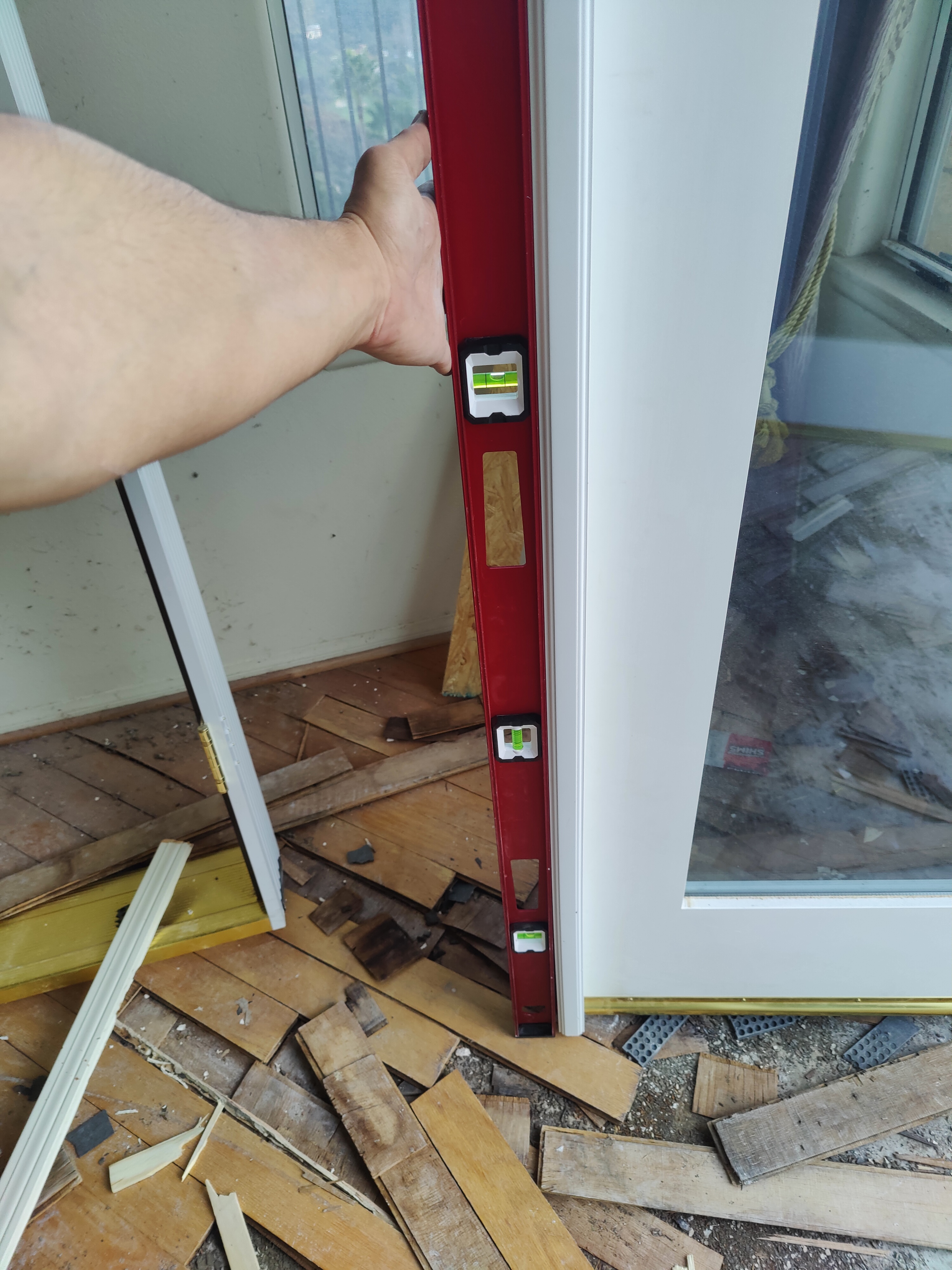 Red spirit level checking plumb on new door frame with wood debris on floor